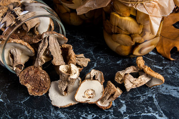 Two glass jars with wild mushrooms on black marble background.