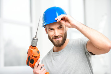 Portrait of a handsome repairman with drill and helmet in the bright interior