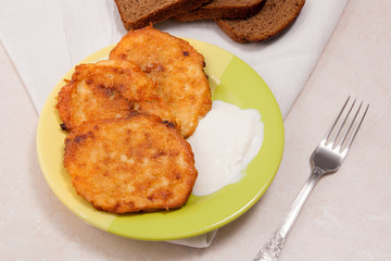 Potato pancakes with meat and sour cream on green plate with rye