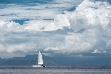 Sail boat moves in the sea with clouds and mountains on the background