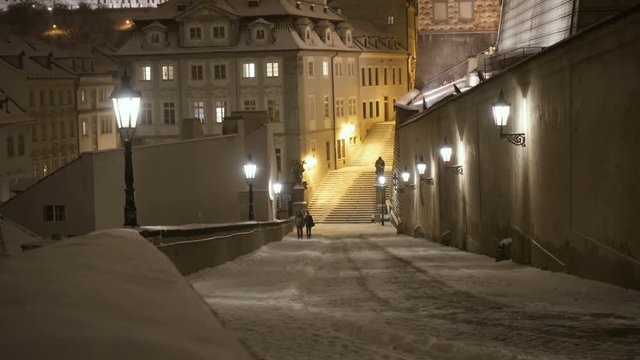 Couple Walking Under a Heavy Snowfall in a Street of Prague in Winter at Night
