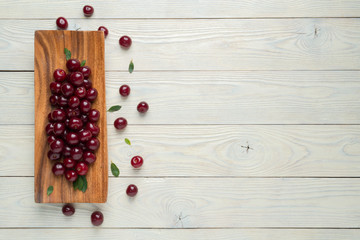ripe cherries and leaves in a wooden plate on a textured wooden background, view from above