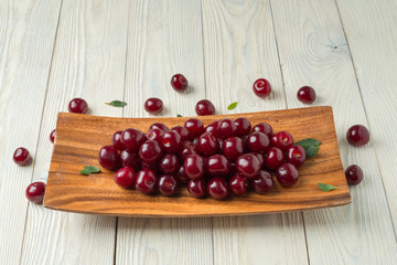 ripe cherries and leaves in a wooden plate on a textured wooden background