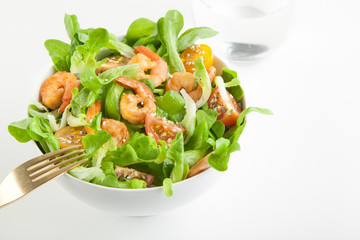 Shrimp salad with cherry tomatoes in bowl on white background with a glass of water. Copy space.