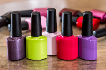 Group of bright nail polishes on wooden desk.