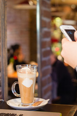 Taking picture of latte coffee with smartphone in cafe