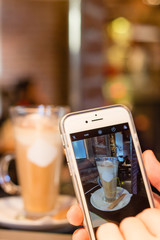 Taking picture of latte coffee with smartphone in cafe
