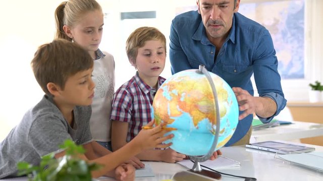 Teacher with kids in geography class looking at globe