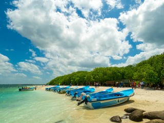 Fototapeta na wymiar Boats on White Sand Sandy Rock Beach Shallow Turquoise water with waves in Pigeon Island Beach with Blue Sky and White clouds and Greenery
