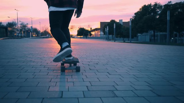 Beutiful and soft pink pastel lighning at winter time. Following camera with close up on skater legs, skating his longboard in city street into sunset