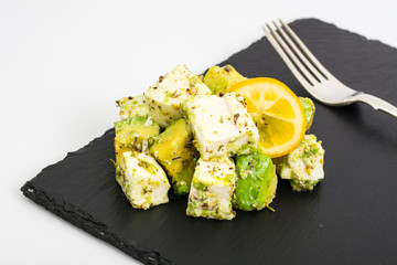 Appetizer with avocado and cheese with herbs on black stone