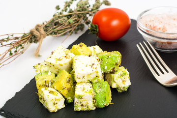 Appetizer with avocado and cheese with herbs on black stone