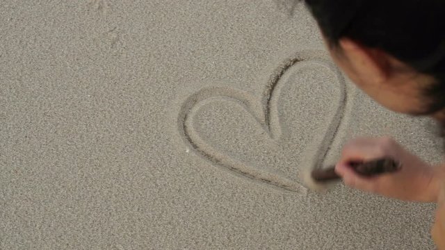 Asian woman drawing heart symbol on sand beach