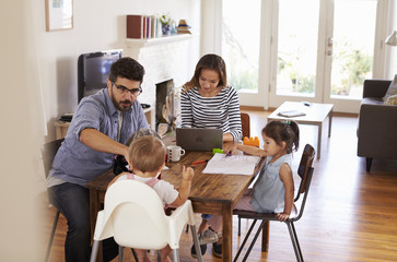 Mother Uses Laptop Whilst Father Plays With Children At Home