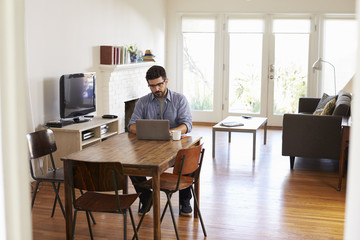 Man Working From Home Using Laptop On Dining Table