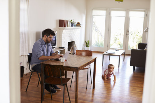 Father Uses Laptop Whilst Baby Son Plays On Floor
