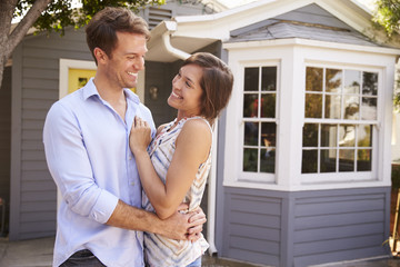 Portrait Of Excited Couple Standing Outside New Home