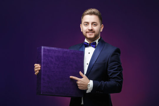 Handsome Man With Beard In Tuxedo Holds Large Box And Smiling On