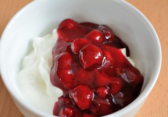 White cream yogurt with red berries fruit in white bowl.