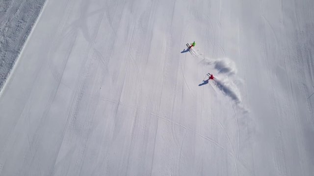 4k footage, top aerial drone view two skiers skiing on empty ski slope in clouds of snow
