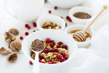 Healthy breakfast: muesli with walnuts, milk, honey and fresh cranberries on white wooden background. Selective focus