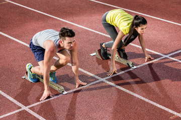 Sportler und Sportlerin in Startposition auf Startblöcken von Aschenbahn