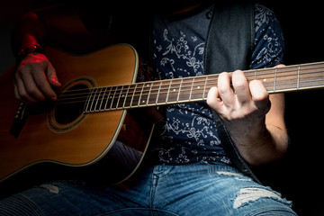 Male hand clamped chord on the acoustic guitar, close-up, on a black background