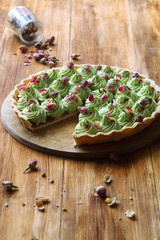 Wild Strawberry Pistachio Tart decorated with dried rose buds on wooden round board, on wooden table.