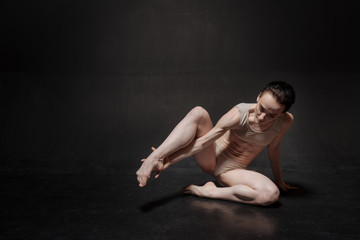 Fototapeta na wymiar Unemotional young ballet dancer stretching in the studio