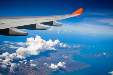 Airplane view of the wing of the plane Ocean island and clouds