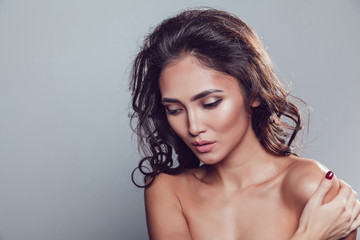 Naklejka premium Brunette girl with shiny wavy hair and beautiful make up posing at studio on grey background.