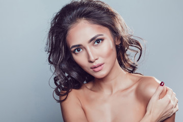 Brunette girl with shiny wavy hair and beautiful make up posing at studio on grey background.