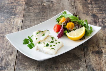 Fried cod fillet and salad on wooden table

