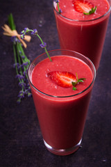 Berry smoothie garnished with strawberries and lavender flowers on dark wooden background. View from above, top studio shot