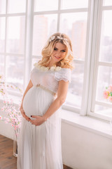 Pretty pregnant woman in white, long dress. Waiting for baby. Fashionable toning