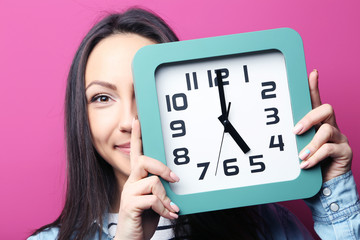 Young woman holding a clock on pink background