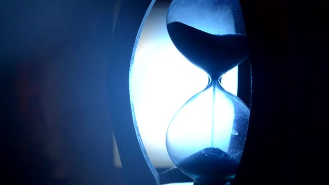 ime concept. Silhouette of Hourglass clock and old vintage wood clock with arrow and smoke on dark background with hot yellow orange blue cold back lighting, or symbols of time under smoke, the end