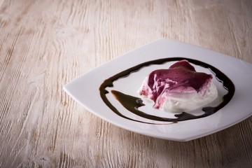 Creamy dessert with berry sauce and chocolate topping on white plate