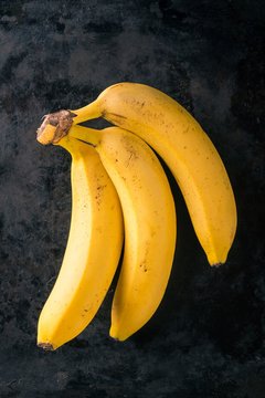 Three yellow bananas on dark worn tray