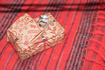 Just for you! A small box containing a present is lying on a red blanket on the left side of the photograph with space for writing is on the right side. 	
