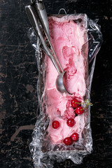 Homemade cherry sorbet in vintage iron container with polyethylene film, fresh cherry berries and metal spoon for ice cream over old black wooden textured background. Top view with copy space