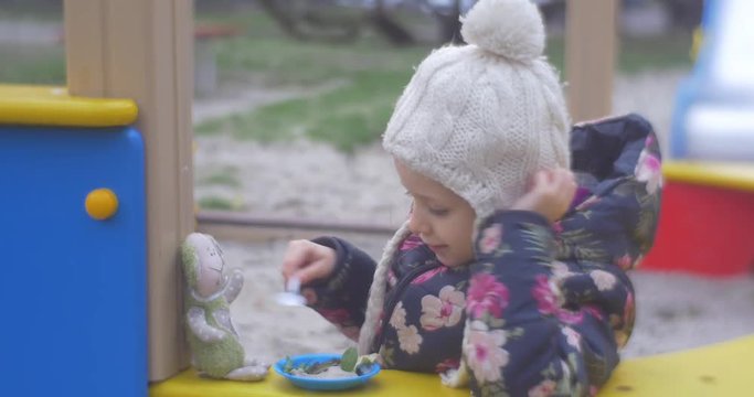 Girl on Playground Feeds Toy Rabbit.
