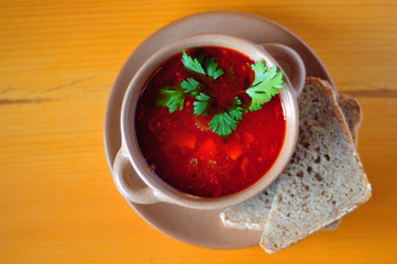Pepper soup in bowl on wooden table with bread, view from top