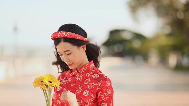 Beautiful Vietnamese girl in red traditional dress Ao Dai with yellow flowers.