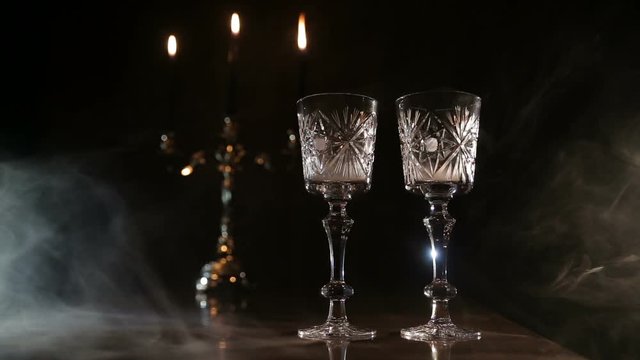 Mystical atmosphere in a dark room with candles, glasses and smoke.Two glasses and candle light at the restaurant.Romantic atmosphere withTwo wine glasses,burning candles in a chandelier.