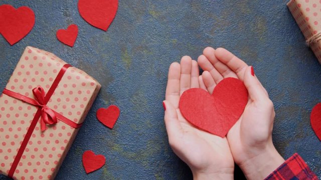Woman's hands holding red heart Valentine's Day surprise symbol concept of gentle love gift on vintage blue table background. Flat lay top view, dolly slider move.