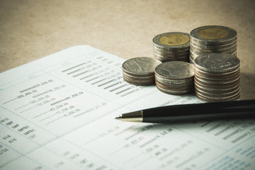 row of coins and pen on account book in finance and banking conc