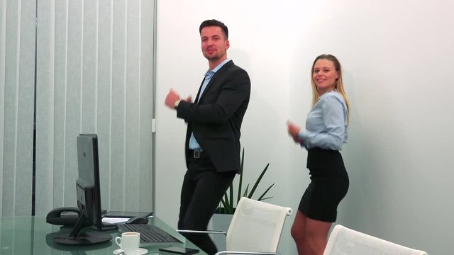 A man and a woman dance in an office and look at the camera