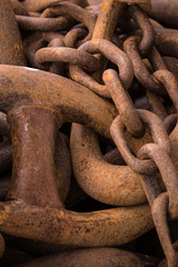 Orkneys, Scotland - June 5, 2012: Closeup of heap of huge rusty heavy metal chain links on the pier of the Stromness harbor. All reds and browns. Three sizes of links.