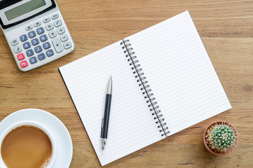 Wooden desk table with notebook, pen, calculator and cup of coff
